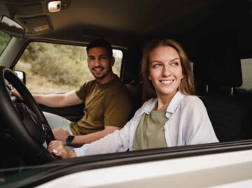 Beautiful young couple sitting on front passenger seats and driving a car